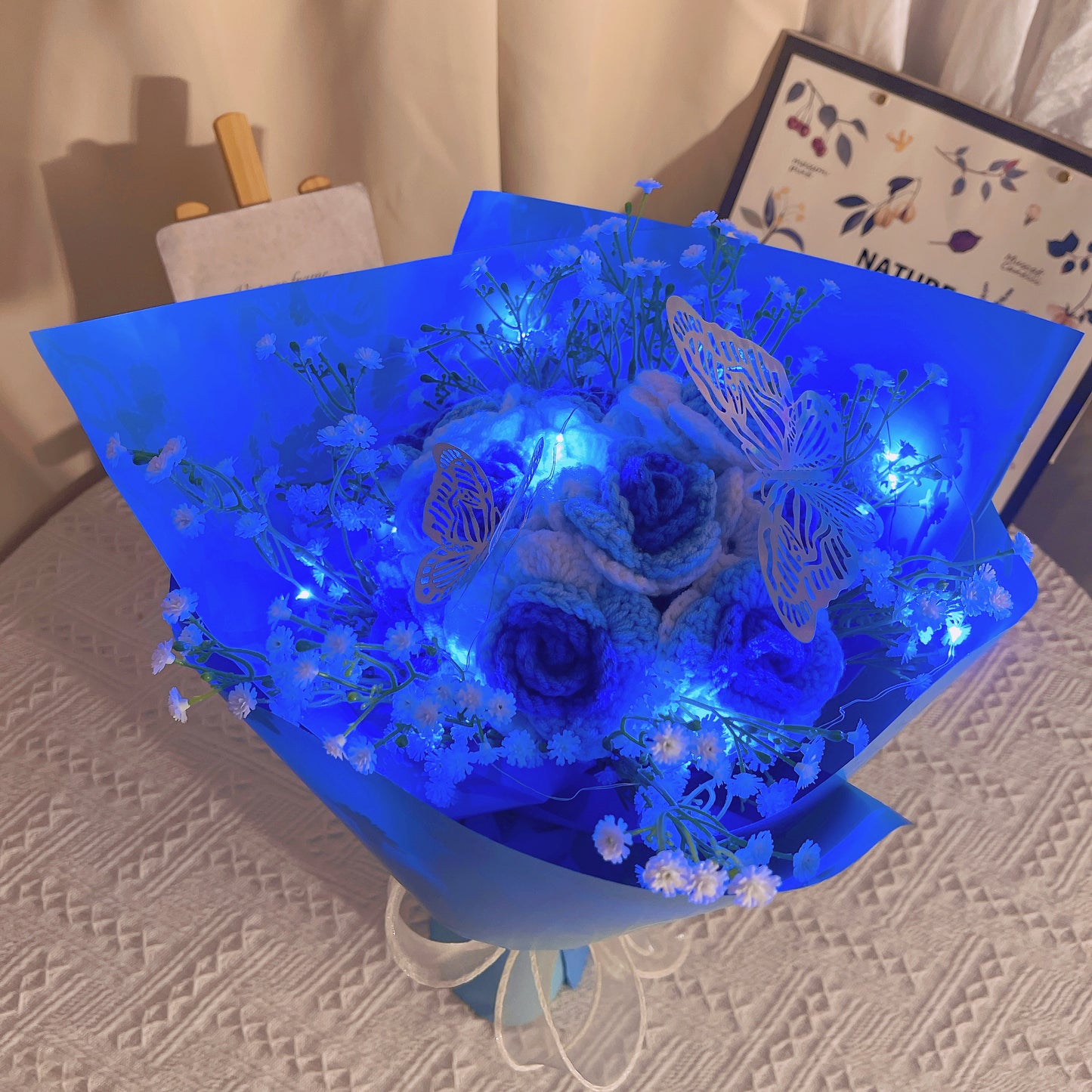 Gefrorener Rosenstrauß mit Farbverlauf von Weiß nach Blau, weißem Schleierkraut und leuchtend bunten Schmetterlingsakzenten, wunderschön verpackt in hell- und dunkelblauem Papier, ideal für Feiern im Prinzessinnenstil.