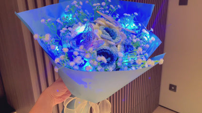 Gefrorener Rosenstrauß mit Farbverlauf von Weiß nach Blau, weißem Schleierkraut und leuchtend bunten Schmetterlingsakzenten, wunderschön verpackt in hell- und dunkelblauem Papier, ideal für Feiern im Prinzessinnenstil.